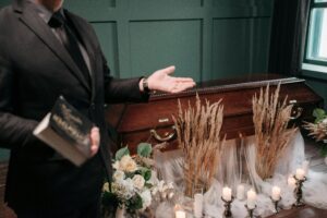 A respectful funeral setting with a closed coffin, flowers, and a man holding a book.